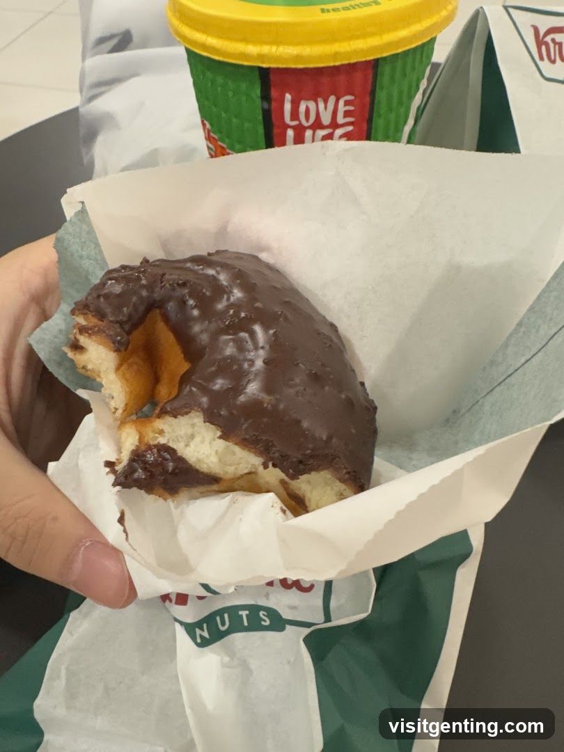 Hand holding chocolate-frosted donut with coffee cup in background