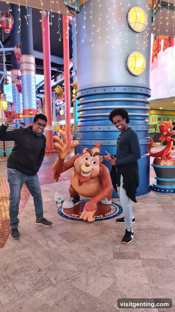 Two people posing with cartoon statue in indoor amusement area