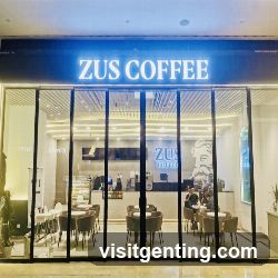 Modern glass facade with illuminated blue sign displaying 'ZUS COFFEE'. Interior visible through large windows showing seating area, counter, and staff at work. Logo and name also appear on the interior wall behind the counter.