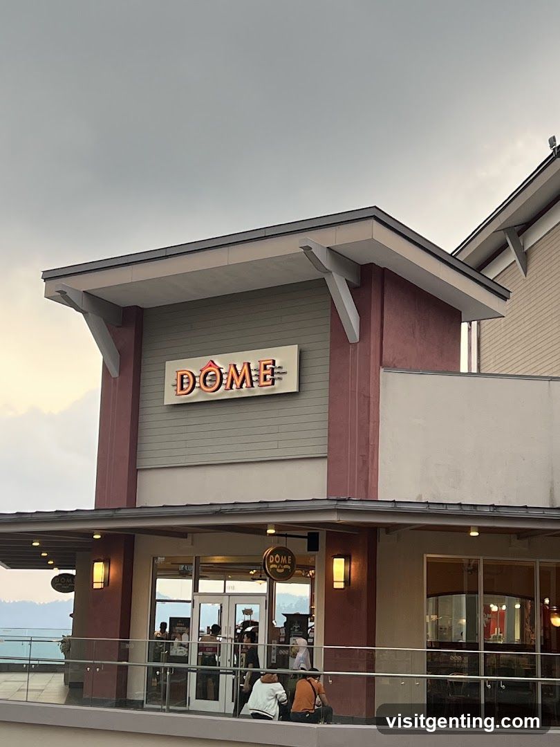 Exterior view of a modern building with a prominent 'DOME' sign above the entrance. The facade features red and gray panels with overhanging eaves. Glass doors and windows show interior lighting. A few people are seated outside on a balcony with glass railings, under an overcast sky.