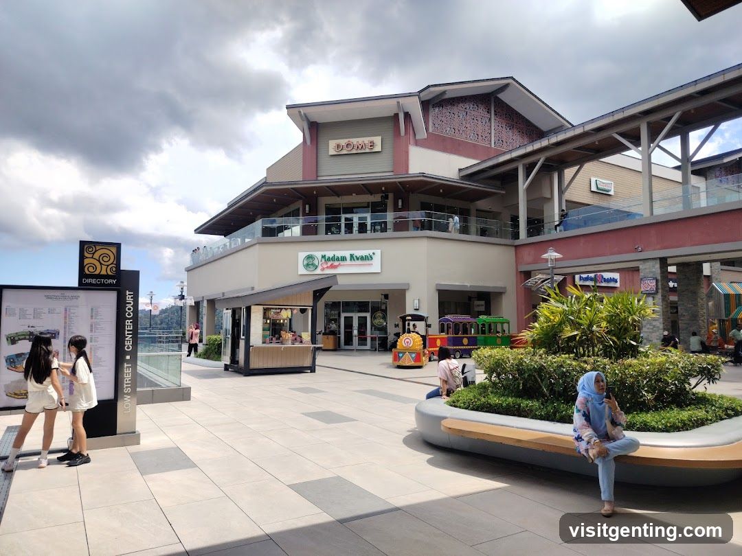 Exterior view of a multi-level shopping center with 'DOME' signage above the main entrance. Below it, 'Madam Kwan's' is visible on the ground floor facade. A small kiosk stands beside the entrance. The building features modern architecture with glass railings and decorative panels.