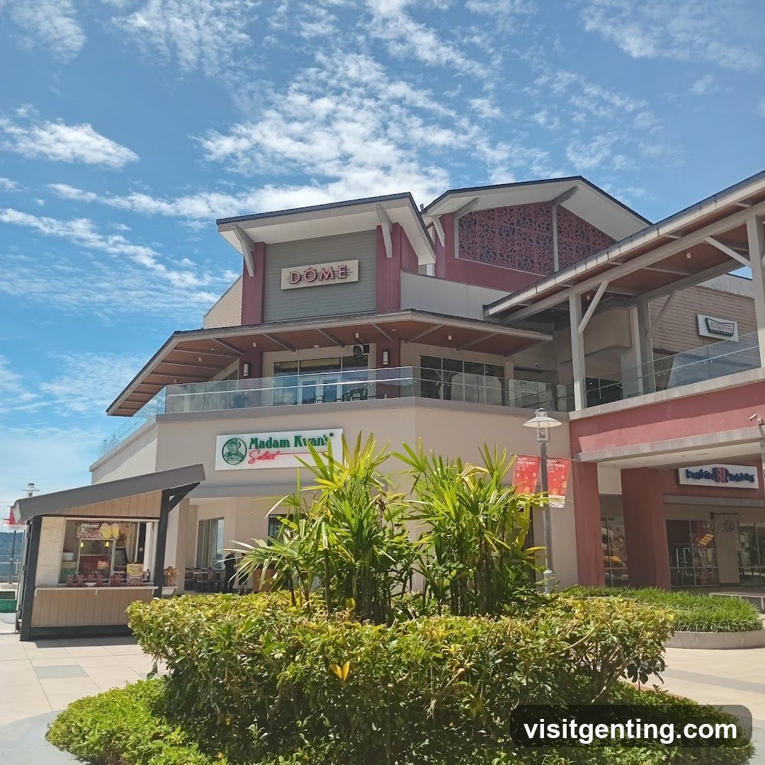 Multi-level commercial building with 'DOME' signage on upper facade, featuring glass railings and decorative red lattice panels. Ground floor includes 'Madam Kyan's Salad' storefront with green logo and white sign, alongside other retail units including one labeled 'Indian Baking'. Lush tropical plants and shrubs in foreground under bright blue sky with scattered clouds.