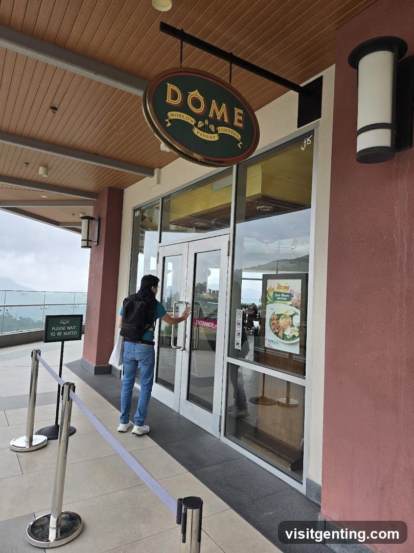 Exterior view of a coffee shop entrance with a circular green and gold sign reading 'DOME' above the glass doors. A person in jeans and a backpack is entering the establishment. The building has wooden paneling on the ceiling, pink walls, and metal stanchions with a rope barrier. A small sign reads 'PLEASE WAIT TO BE SEATED'. Reflections show interior seating and a promotional poster inside.